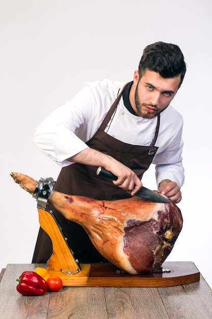 Cook in apron cuts appetizing ham, isolated on white space,