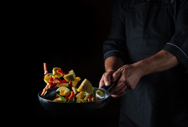 Cook bereidt groenten in koekenpan Koken gezond vegetarisch eten en maaltijd op een donkere achtergrond