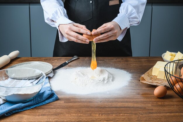 料理人は、材料と一緒にテーブルの上で卵をベーキング小麦粉に砕きます。