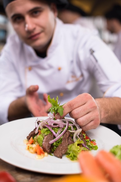 cook chef decorating garnishing prepared meal dish on the plate in restaurant commercial kitchen