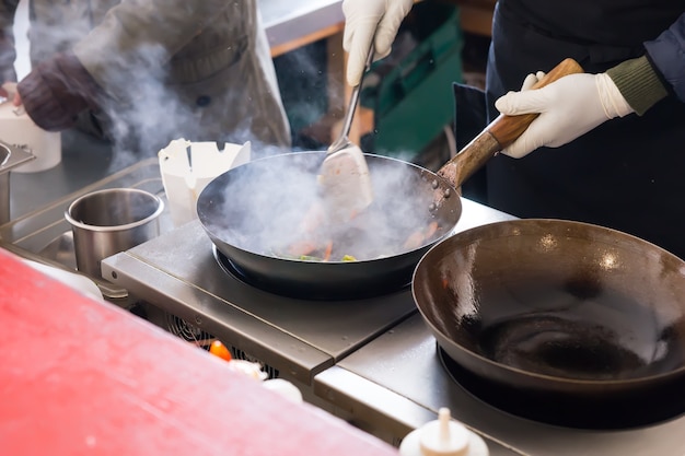 Cuocere o cuocere lo chef su una piastra elettrica in una cucina commerciale con una nuvola di vapore sopra una grande padella