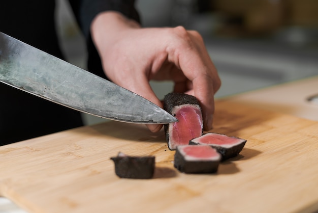 木製の大皿に中くらいの珍しいマグロのグリル肉をナイフで切る