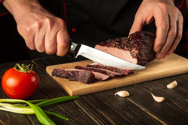 The cook cuts the baked veal meat on a cutting board