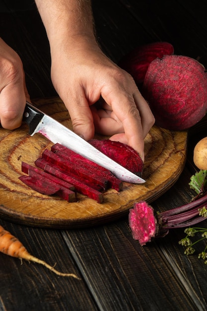 The cook cuts beetroot with a knife to prepare delicious borscht Ukrainian national cuisine