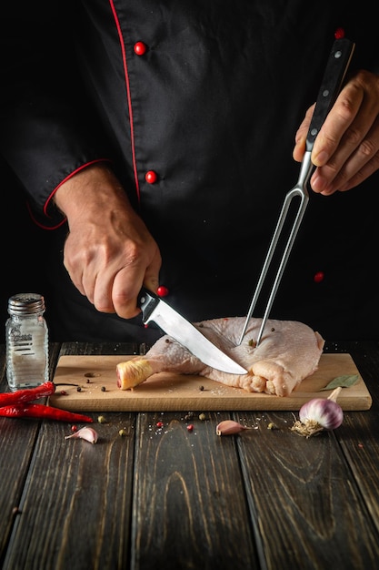 Photo the cook cuts the chicken leg with a knife in the kitchen