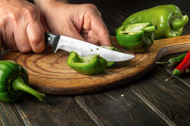 料理人は、木製のまな板に新鮮なピーマンをカットします 菜食主義の食糧を準備しながらシェフの手のクローズ アップ