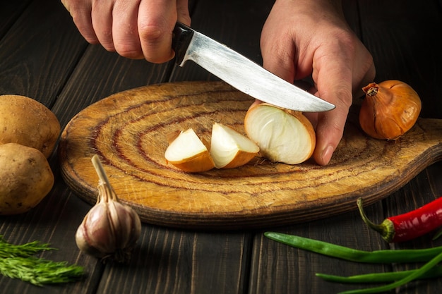 Il cuoco taglia la cipolla con un coltello su un tagliere per fare la zuppa per il pranzo