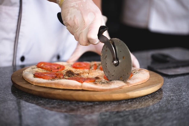 The cook cuts pizza with a round knife