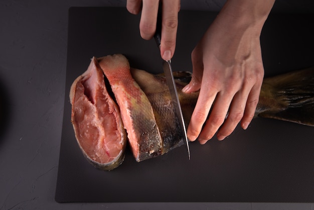 사진 요리사는 회색 보드에 칼로 물고기를 조각으로 잘라냅니다.