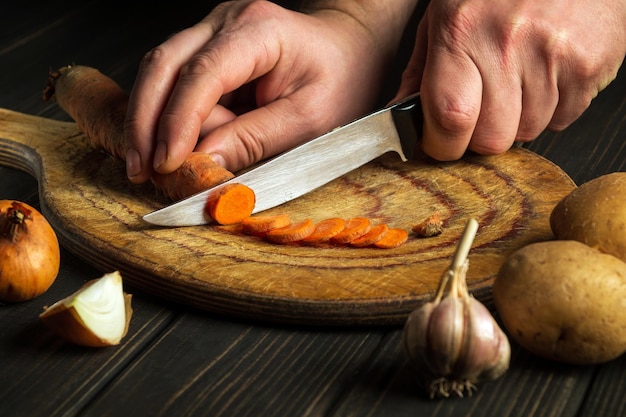 Il cuoco taglia le carote per la zuppa di verdure su un tagliere