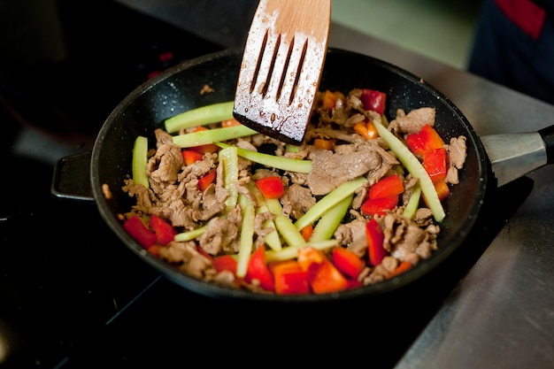 Cook fries meat in a pan with vegetables