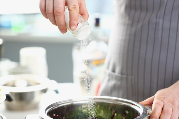 Cook giet zout in de pan in de keuken