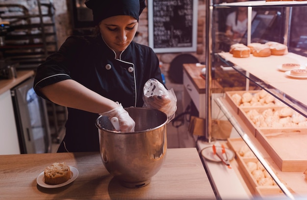 A cook girl in a black suit puts cream in a pastry bag the pastry chef puts cream in a cooking bag