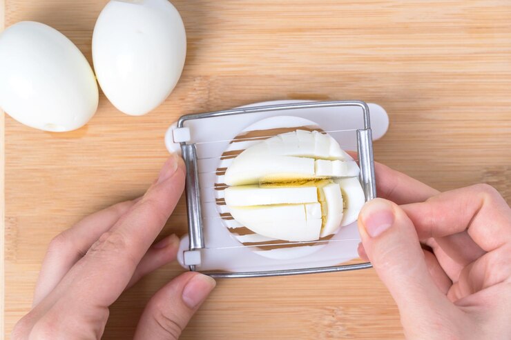 Повар измельчает вареные куриные яйца с помощью устройства для резки яиц, вид сверху