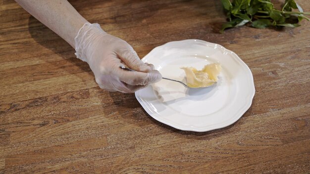 Cook hand in glove serving cooked tortellini on white plate wooden table