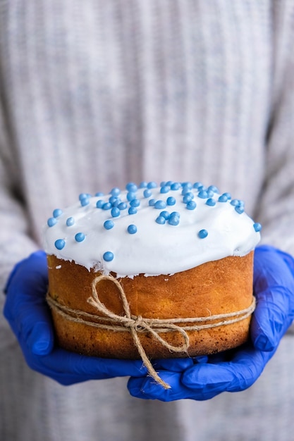 The cook Hands in blue gloves hold Easter cake with white topping and blue sprinkles Woman holding traditional Russian Easter cake Homemade pie for spring holiday celebration