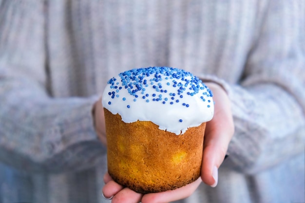 料理人の手は白いトッピングと青い振りかけるイースターケーキを保持します伝統的なロシアのイースターケーキを保持している女性春の休日のお祝いのための自家製パイ