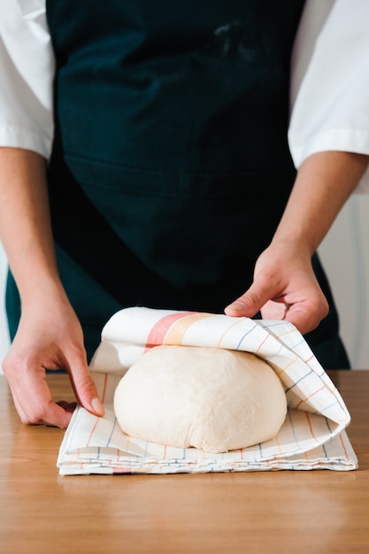 Cook hands kneading dough, sprinkling piece of dough with white wheat flour.