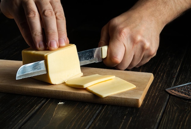 The cook hands with knife cutting a cheese on the wooden board for sandwich italian pizza or snack in the kitchen Preparation for cooking Healthy eating and lifestyle Food concept