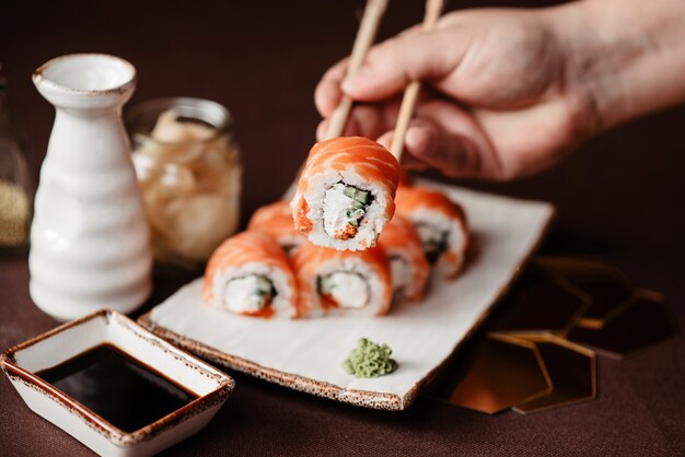 Photo the cook holds with the chopsticks sushi roll with salmon meat