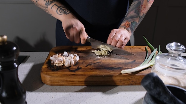 Foto il cuoco sta tagliando finemente l'aglio su un tavolino di legno in cucina