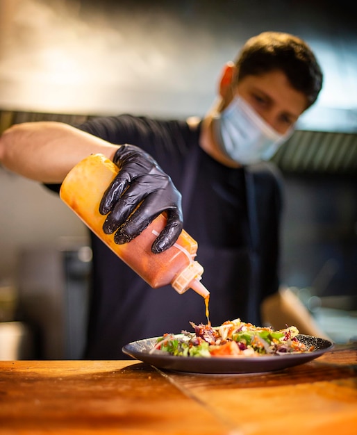 Cook in the kitchen of a restaurant adding sauce to a salad