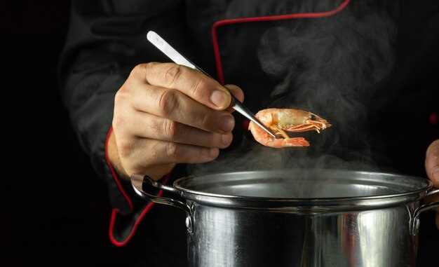 The cook in the pot prepares shrimps The chef checks the readiness of the shrimp Kitchen tool in the chefs hand