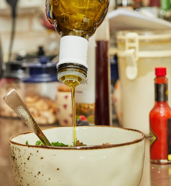 Premium Photo Cook pours oil into salad in deep bowl.