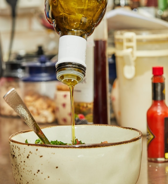 Photo cook pours oil into salad in deep bowl.