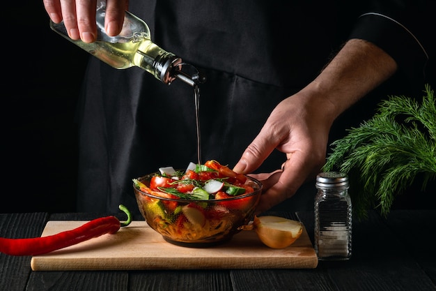 Cook pours olive oil into a bowl of salad