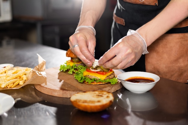 Cook preparing burger adding bacon on the wodden board