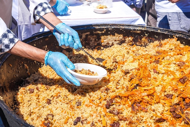 Il cuoco mette il pilaf caldo in un piatto di plastica usa e getta. cibo di strada asiatico