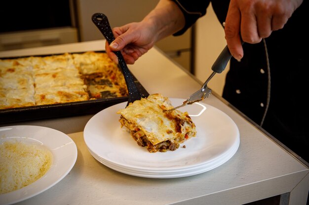 Cook puts a piece of fresh lasagna on a white plate