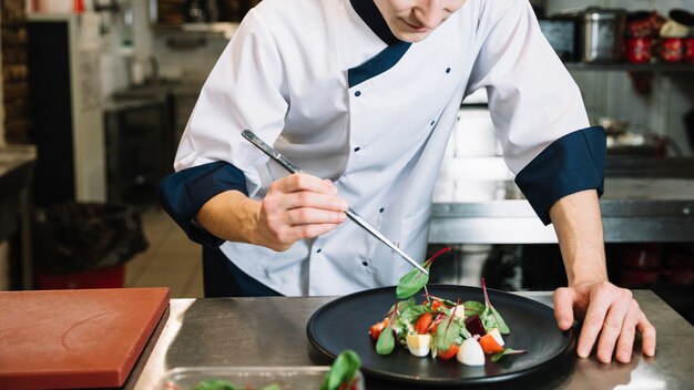 Cook putting spinach on big plate with salad