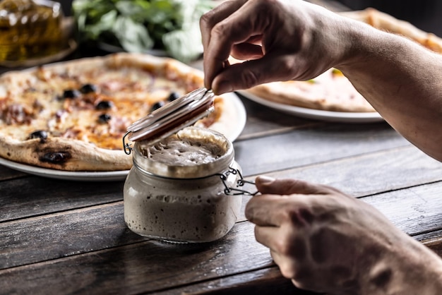 Cook's hands open a jar of rye sourdough in the background a pizza made with sourdough