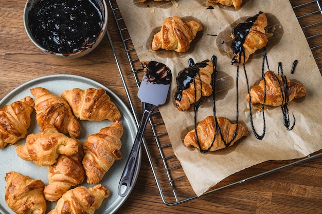 The cook spreads a croissant with chocolate on a wooden table.