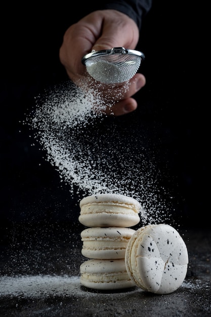 Cook sprinkles macaroon on black background. Close up.