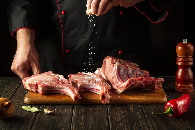 The cook sprinkles raw ribs with salt The concept of cooking delicious food for the hotel