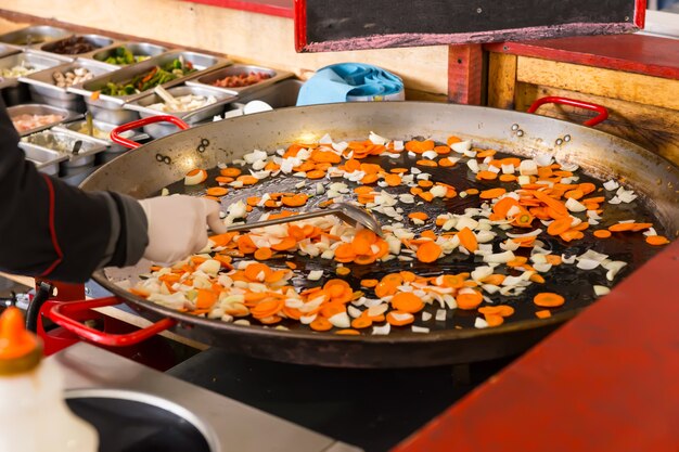 Cook stir frying fresh vegetables in a large pan on a buffet moving the diced veggies with a spatula