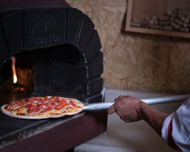 Photo cook taking pizza out of clay oven with flames