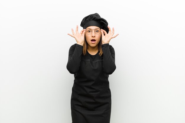 Cook woman feeling shocked, amazed and surprised, holding glasses with astonished, disbelieving look