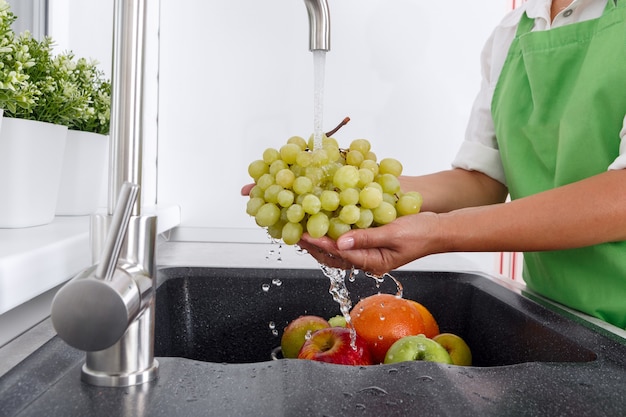 Cook woman washes a bunch of grapes under the water flowing from a tap.