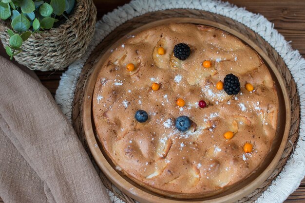 A cooked apple pie on a wooden background decorated with a physalis flower blackberries and cranberries Apple charlotte