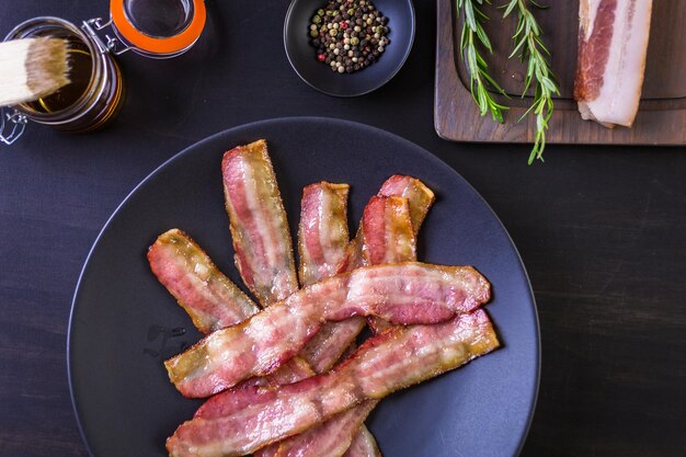 Cooked bacon strips on a black plate.