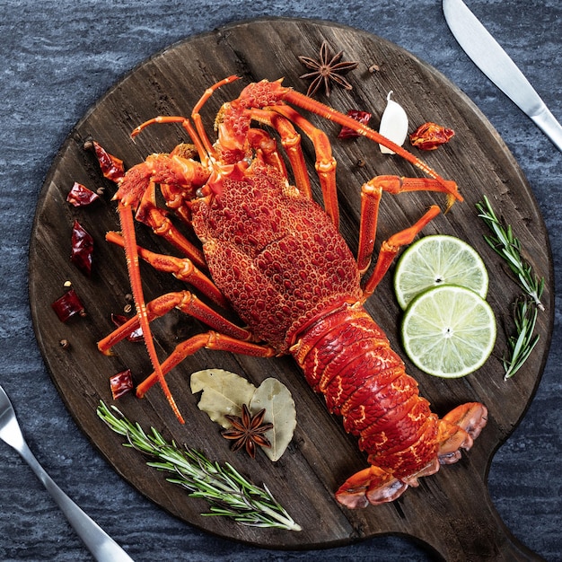 Cooked boiled lobster delicious dinner seafood meal set with\
knife and fork on black stone slate background restaurant menu\
design top view overhead