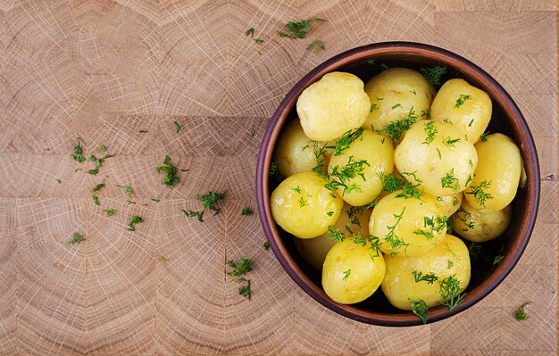 Cooked boiled potatoes with dill in bowl on wooden board. Top view