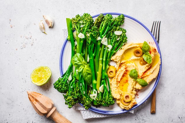 Cooked broccolini with hummus on a white plate, top view. 