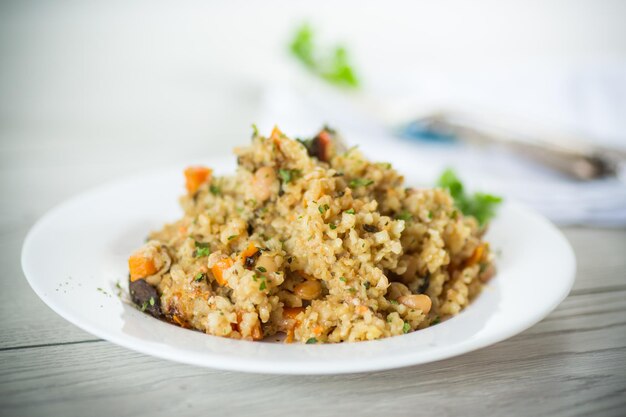 cooked bulgur with vegetables carrots and dried mushrooms in a plate on a wooden table