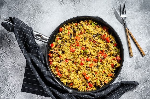 Cooked bulgur with vegetables in a pan. Gray background.