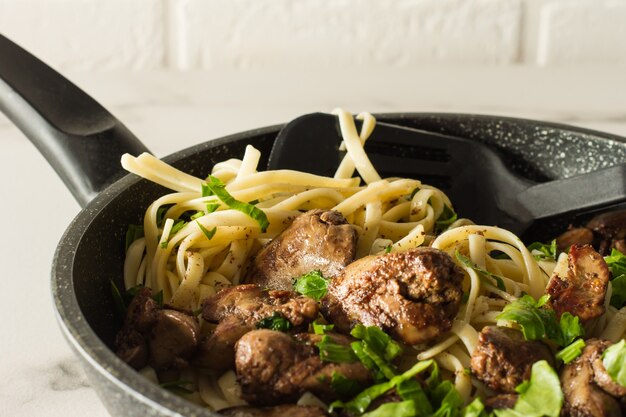 Fegato di pollo cotto con cipolla e spaghetti su una penna di cottura con prezzemolo. cena gustosa in famiglia.